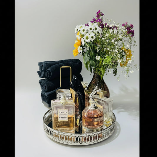 Tray with Chanel and YSL perfumes, a bouquet of flowers, and folded towels on a white background