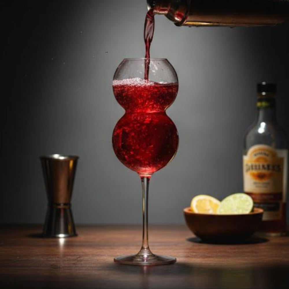 Red liquid being poured into a glass with a bottle and lemons in the background.