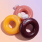 Three donut-shaped bottles with colorful glaze on a pink background