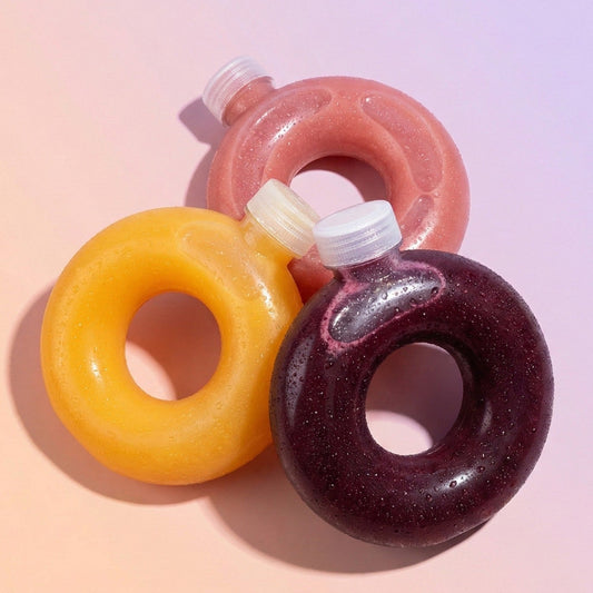 Three donut-shaped bottles with colorful glaze on a pink background