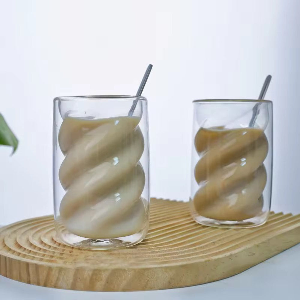 Two glass tumblers with a spiral design filled with a creamy liquid on a wooden surface.