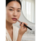 Woman applying lipstick with a dome shape lip brush in a softly lit room.