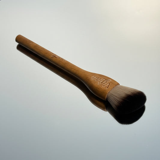 Makeup brush with wooden handle and soft bristles on a reflective surface