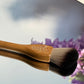 Makeup brush with wooden handle on a reflective surface with blurred flowers in the background