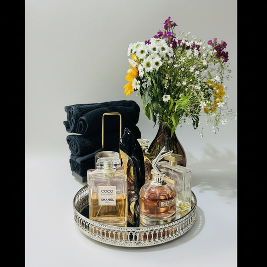 Tray with Chanel and YSL perfumes, a bouquet of flowers, and folded towels on a white background