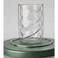 Glass candle holder with wavy design on a green stand against a light gray background