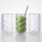 Three glass tumblers with a green smoothie and a metal straw on a white background