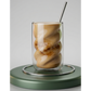 Glass of iced coffee with a metal straw on a green coaster against a gray background