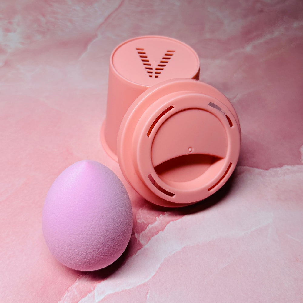 Pink makeup sponge and its lid on a pink marble background