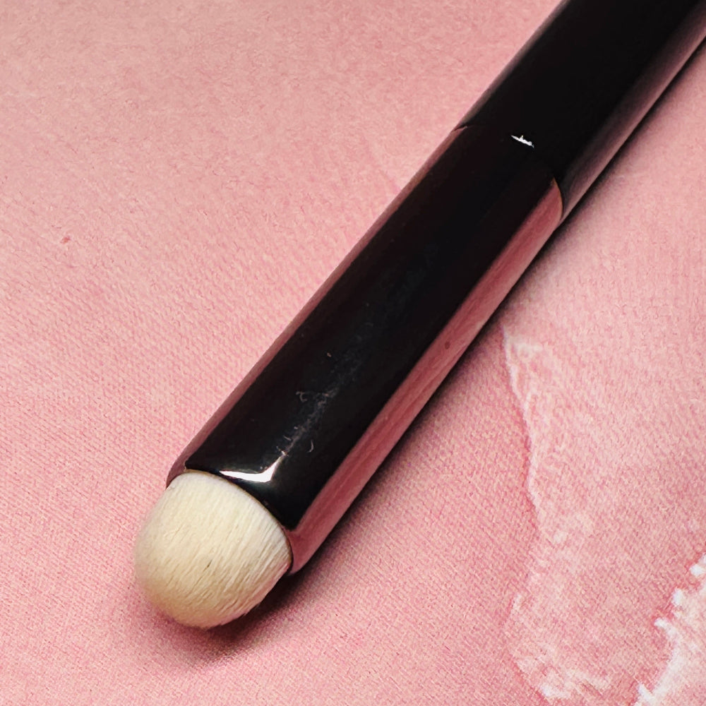 Makeup brush with black handle and beige bristle on a pink textured background