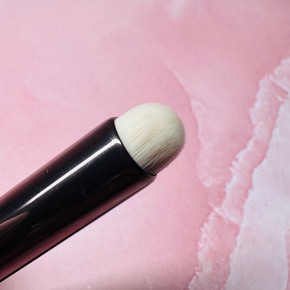 Makeup brush with a white bristle tip on a pink textured background