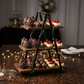 Three-tiered wooden dessert stand with cupcakes, chocolates, and cheesecakes on a wooden surface.