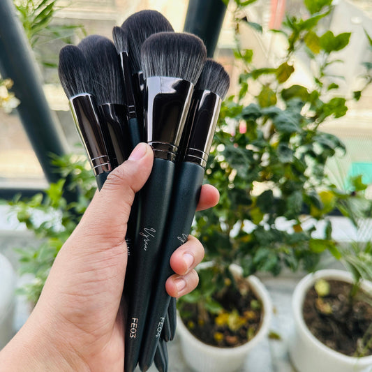 Hand holding a set of black makeup brushes with blurred greenery in the background